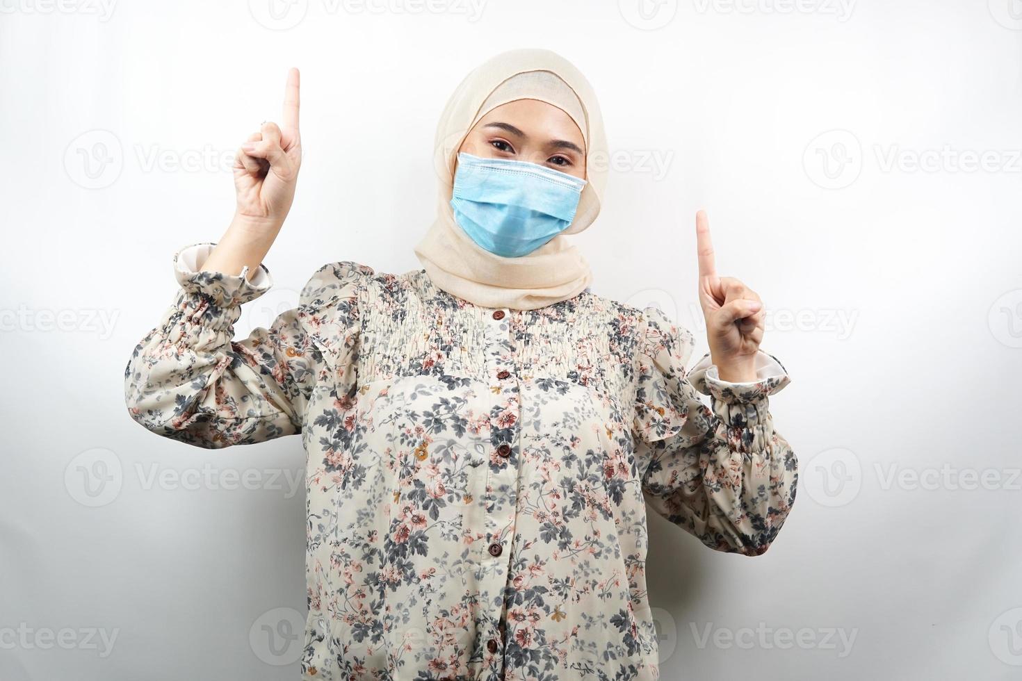 donna musulmana che indossa maschera medica, mano che indica lo spazio vuoto, mano che punta verso l'alto presentando qualcosa, isolato su sfondo bianco foto