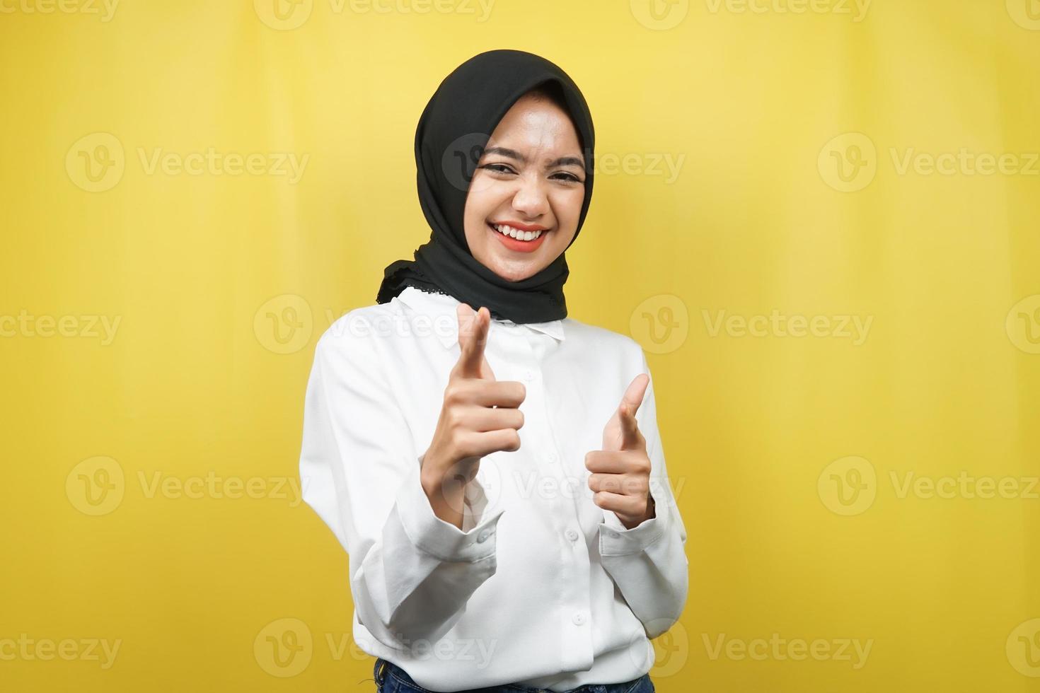 bella giovane donna musulmana asiatica sorridente sicura di sé, entusiasta e allegra con le mani che puntano alla telecamera, le mani che puntano al pubblico, di fronte alla telecamera isolata su sfondo giallo foto