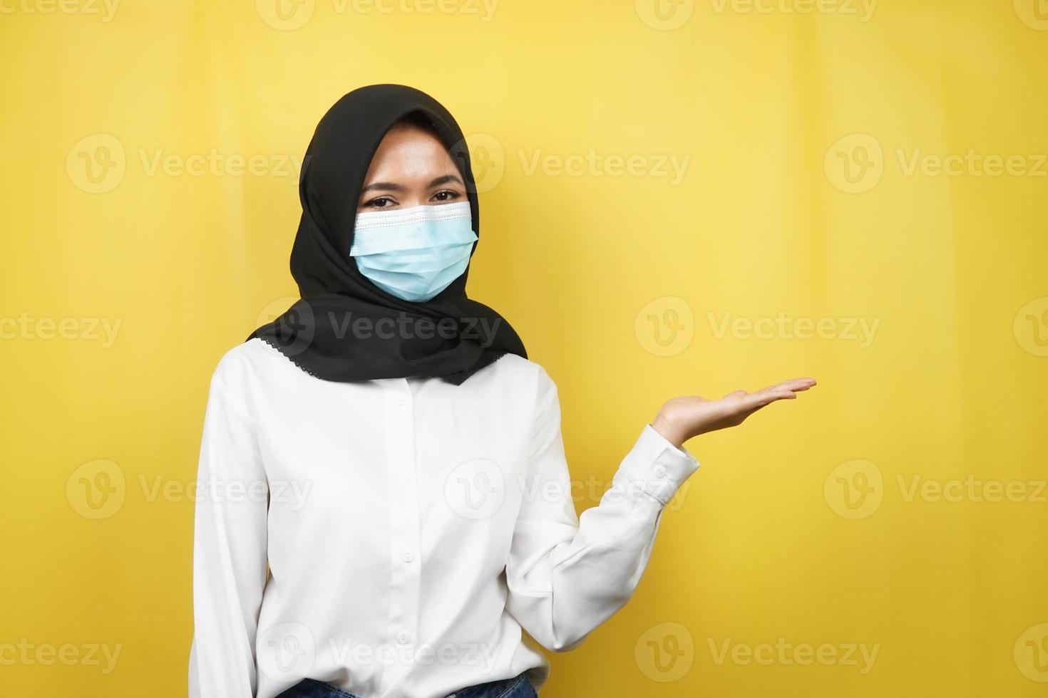 donna musulmana che indossa maschera medica, mani che presentano qualcosa nello spazio vuoto, isolato su sfondo giallo foto