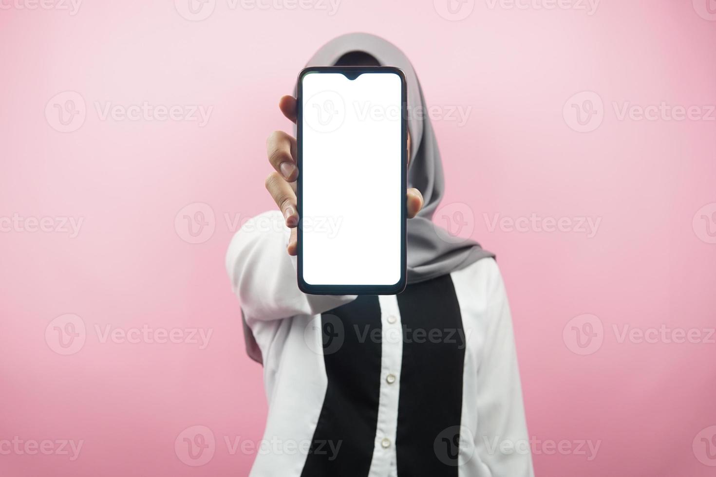 donna musulmana con le mani che tengono lo smartphone, presentando app, presentando qualcosa, isolato su sfondo rosa, concetto pubblicitario foto