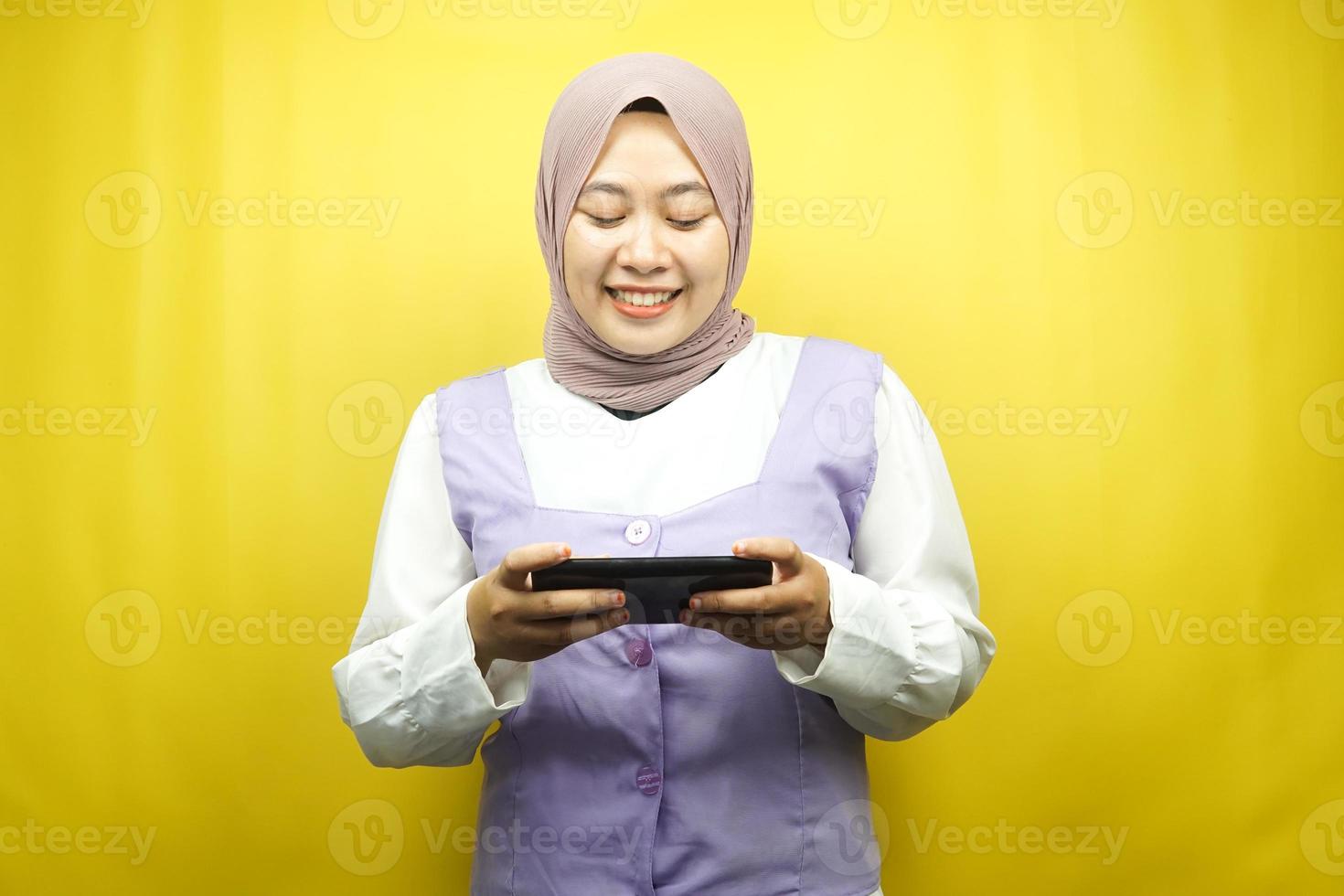 bella giovane donna musulmana asiatica con le mani che tengono smartphone, gioco, sorridente felicemente, vittoria, successo, isolato su sfondo giallo, concetto pubblicitario foto