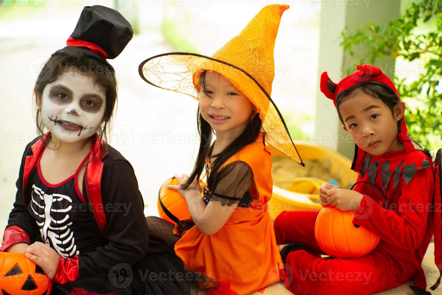 ritratto di sorelle felici in costume di halloween seduto davanti alla porta e in attesa di giocare dolcetto o scherzetto. buon giorno di halloween foto