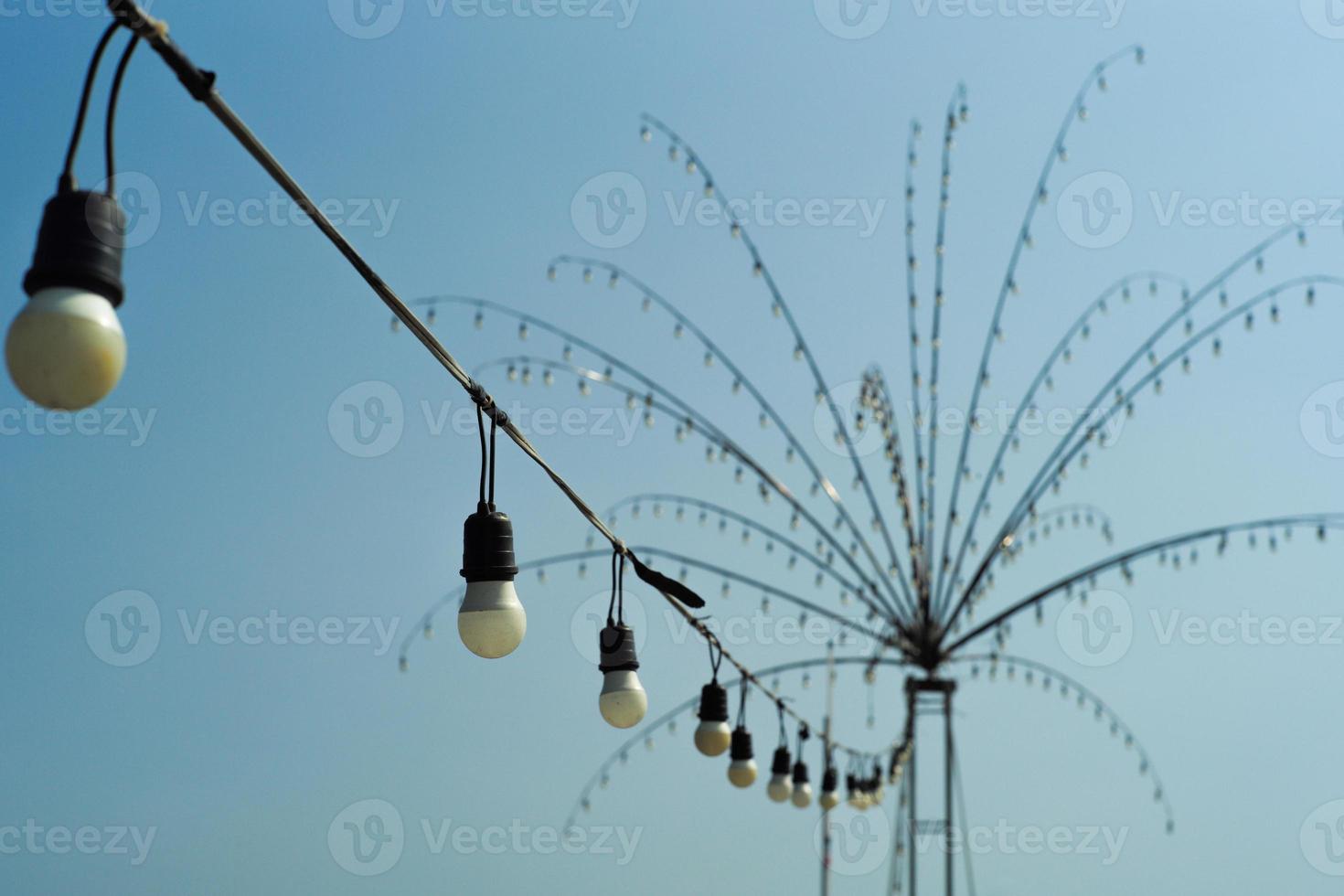 messa a fuoco selettiva sulle lampadine elettriche installate in linea con un gruppo sfocato di lampadine decorate a forma di albero foto