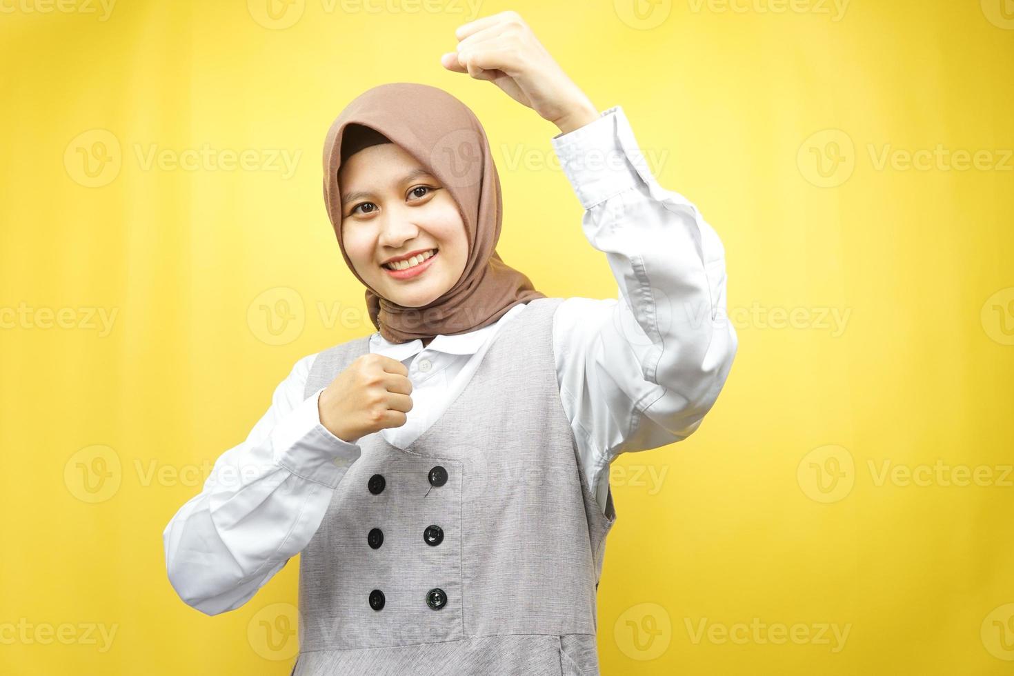 bella giovane donna musulmana asiatica sorridente sicura di sé, entusiasta e allegra con le mani serrate, segno di successo, pugni, combattimenti, non paura, isolata su sfondo giallo foto