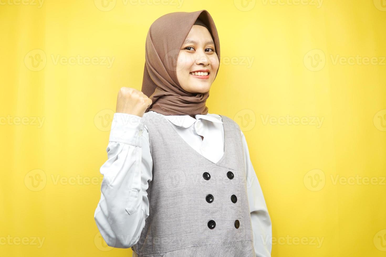 bella giovane donna musulmana asiatica sorridente sicura di sé, entusiasta e allegra con le mani serrate, segno di successo, pugni, combattimento, non paura, vittoria, isolato su sfondo giallo foto
