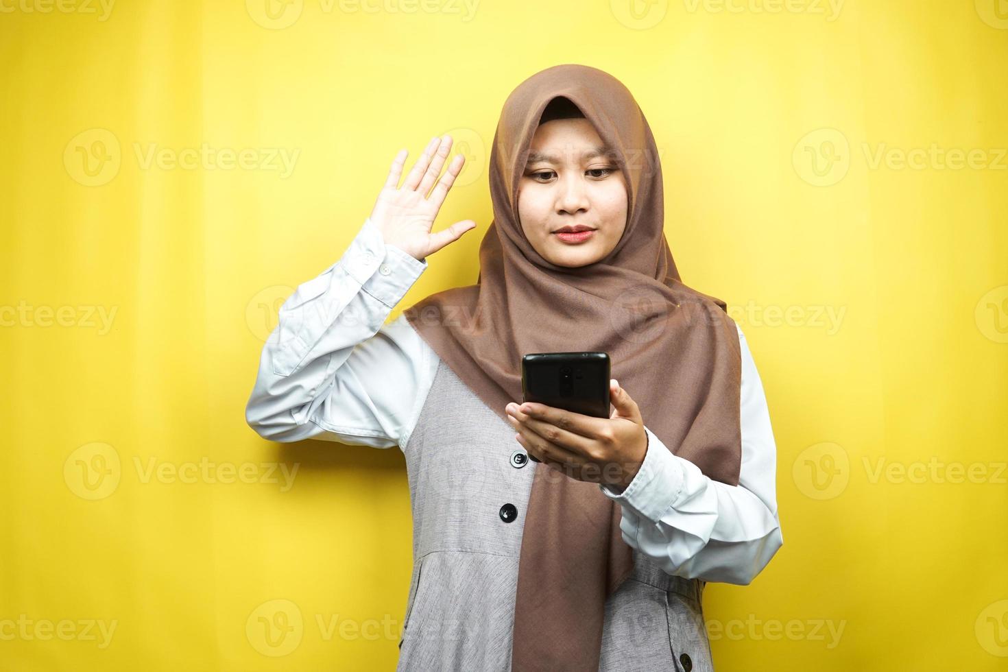 bella giovane donna musulmana asiatica scioccata, sorpresa, con le mani che tengono smartphone, guardando smartphone, guardando promo, isolato su sfondo giallo, concetto pubblicitario foto