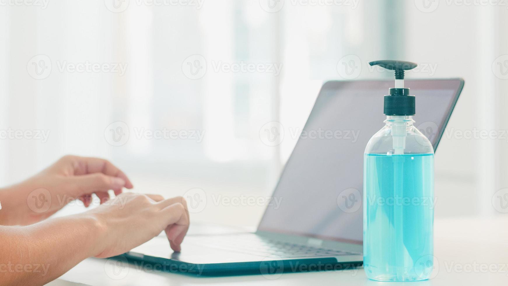 donna asiatica che usa un disinfettante per le mani in gel alcolico lavarsi le mani prima di aprire il laptop per proteggere il coronavirus. le donne spingono l'alcol a pulire per l'igiene quando il distanziamento sociale resta a casa e il tempo di autoquarantena foto