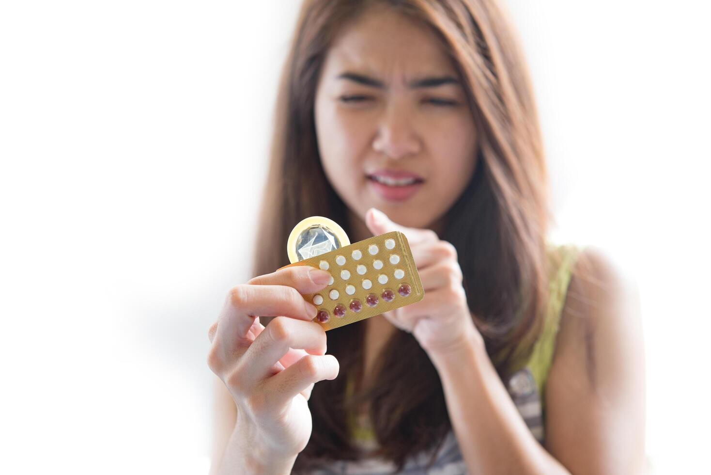 la giovane donna che tiene il preservativo e le pillole contraccettive previene la gravidanza foto