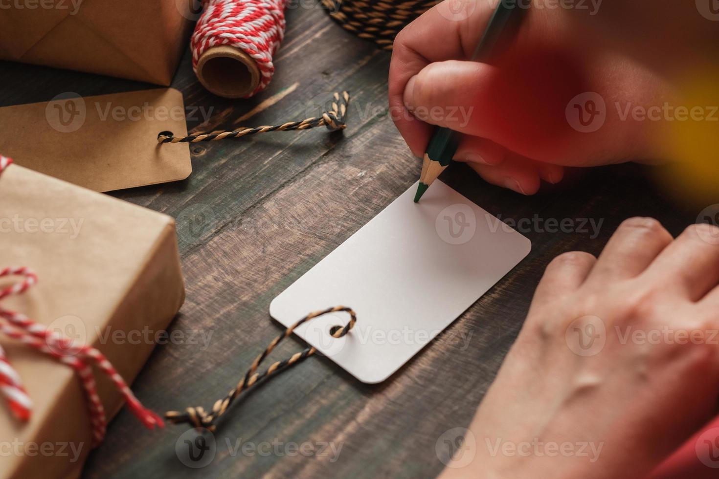 donna che scrive un cartellino regalo e si attacca al regalo di natale su un tavolo di legno foto