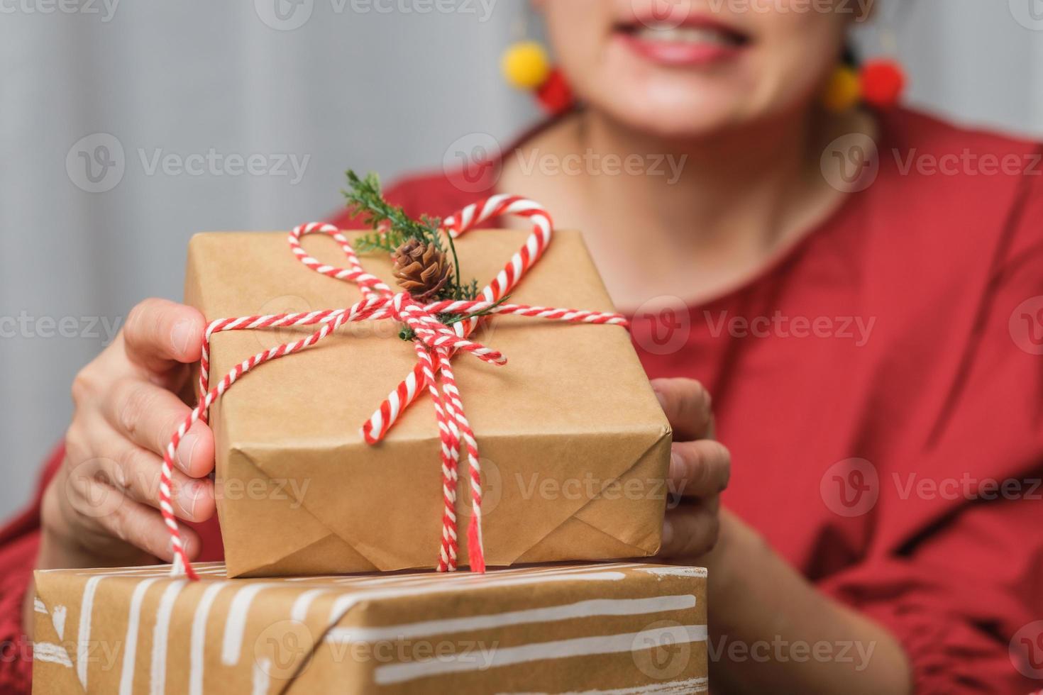 donna che fa una scatola regalo natalizia fatta a mano con carta marrone ordito con decorazioni natalizie su tavola di legno foto