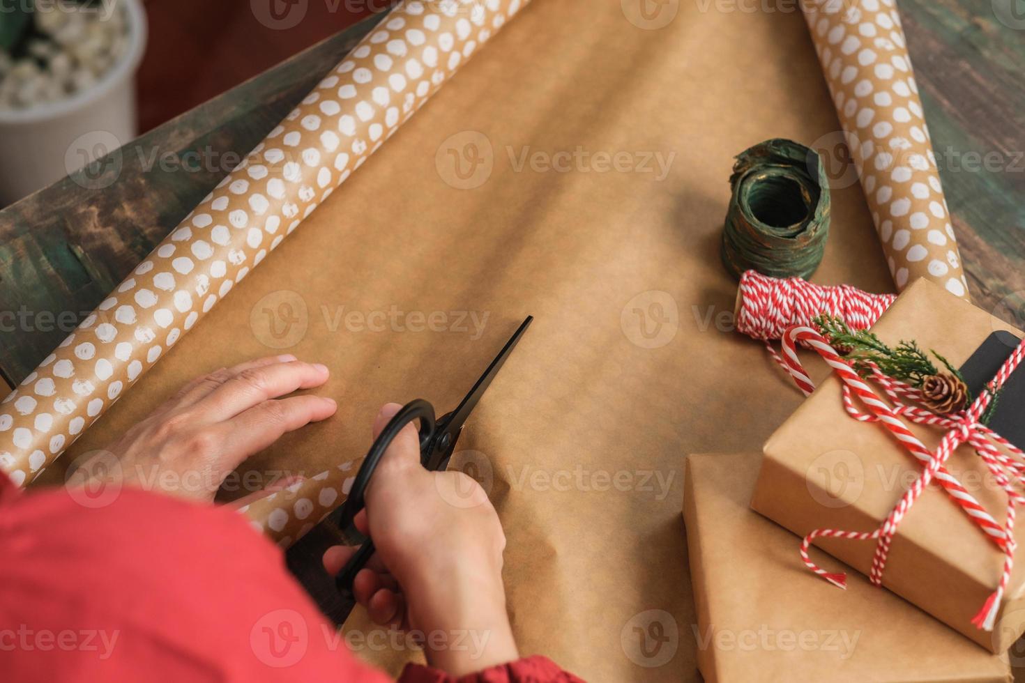 primo piano donna che taglia a mano la carta kraft per avvolgere la confezione regalo di natale su un tavolo di legno foto