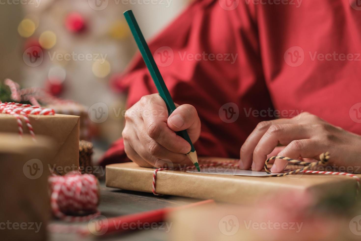 donna che scrive un cartellino regalo e si attacca al regalo di natale su un tavolo di legno foto