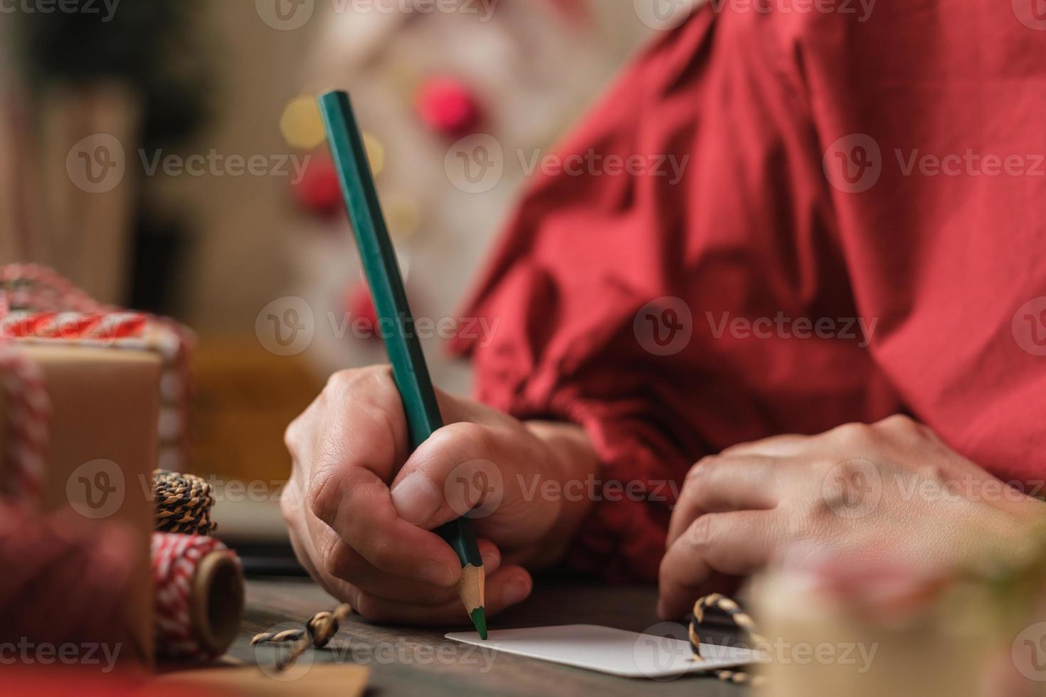 donna che scrive un cartellino regalo e si attacca al regalo di natale su un tavolo di legno foto