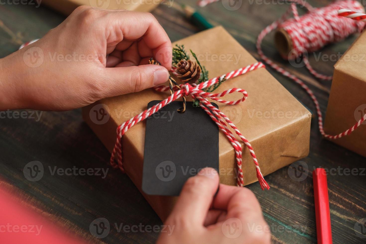 donna che scrive un cartellino regalo e si attacca al regalo di natale su un tavolo di legno foto