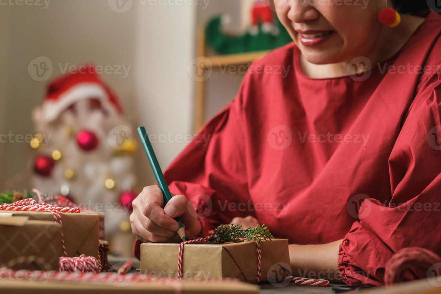 donna che scrive un cartellino regalo e si attacca al regalo di natale su un tavolo di legno foto