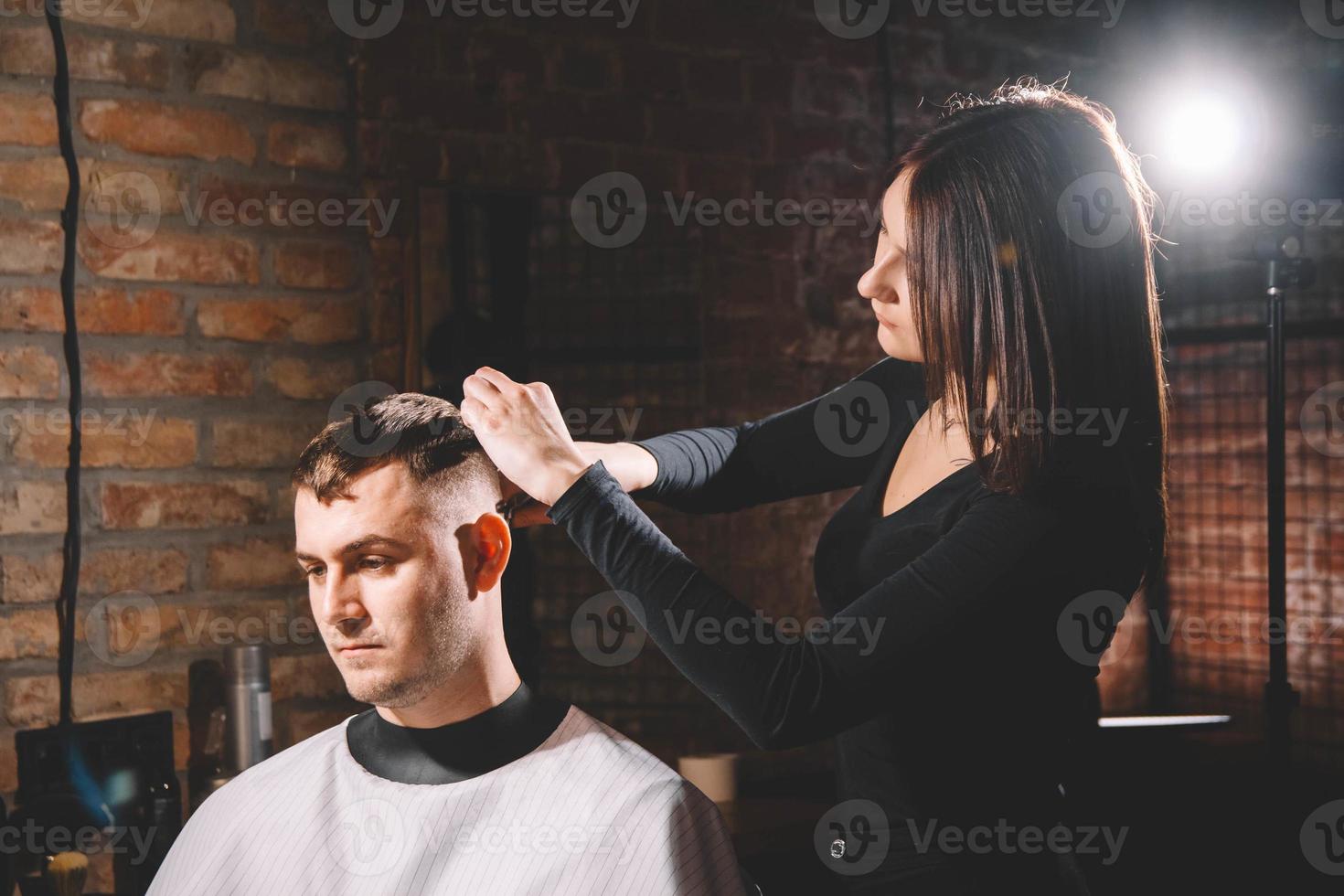 bella femmina parrucchiere taglio dei capelli del cliente con le forbici in un negozio di barbiere foto