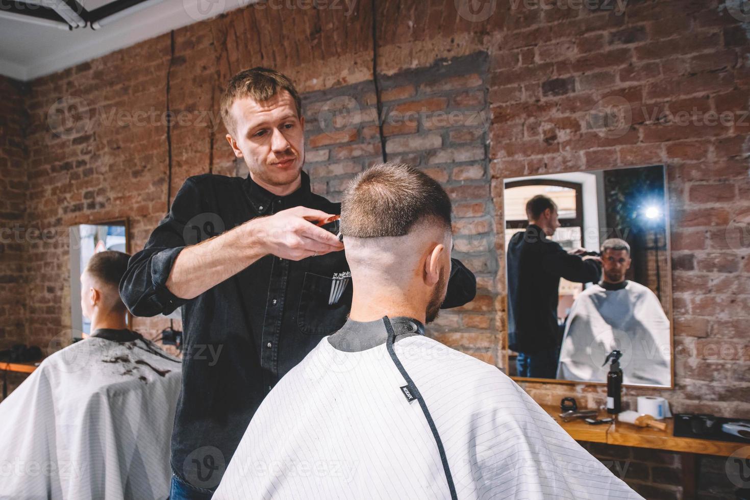 giovane barbiere maschio rade la testa del cliente con un rifinitore elettrico foto