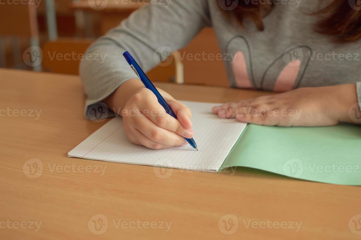 la mano di una ragazza adolescente scrive con una penna a sfera in un terad durante una lezione a scuola foto