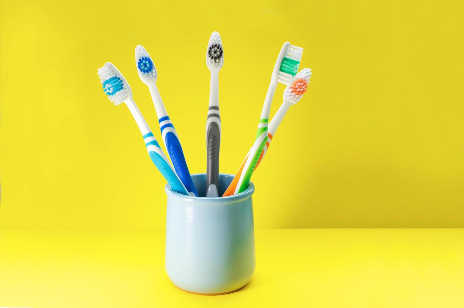 spazzolini da denti multicolori in un bicchiere blu su sfondo giallo. avvicinamento. foto
