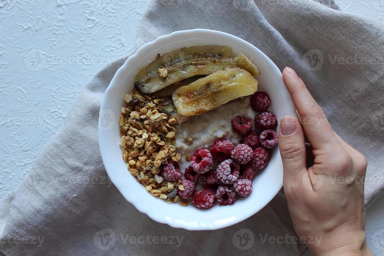 la mano della ragazza tiene un piatto di porridge di farina d'avena con lamponi e banane fritte. colazione salutare. foto