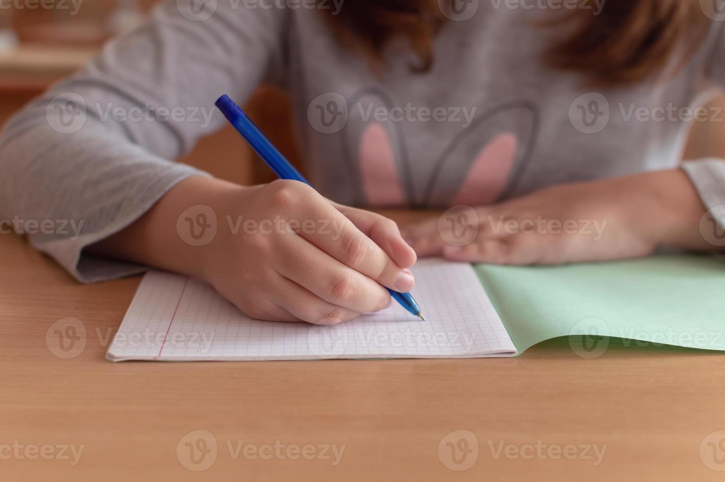 la mano di una ragazza adolescente scrive con una penna a sfera in un terad durante una lezione a scuola foto