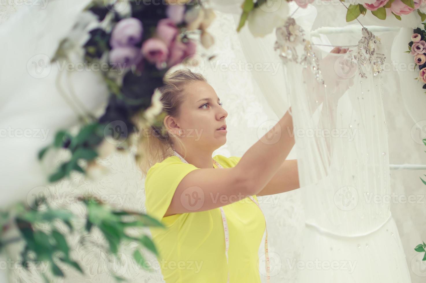 una sarta in un salone di nozze sta preparando un vestito per la vendita. abito da sposa arco da giardino foto