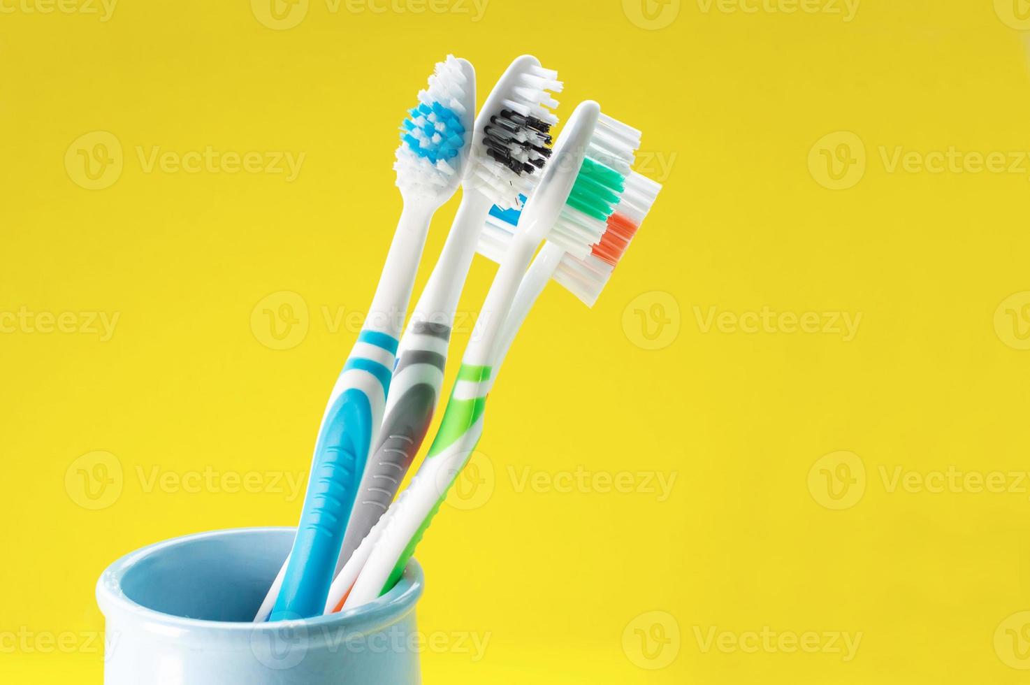 spazzolini da denti multicolori in un bicchiere blu su sfondo giallo. avvicinamento. foto