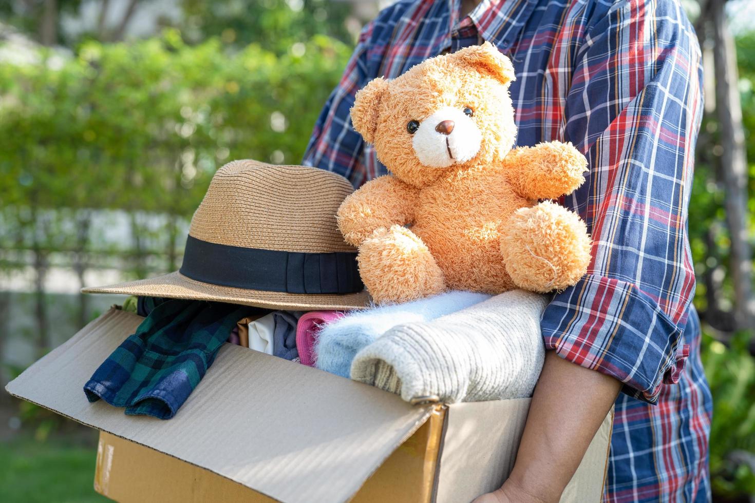 tenendo in mano una scatola per la donazione di vestiti con vestiti usati e una bambola a casa per sostenere l'aiuto ai poveri nel mondo. foto