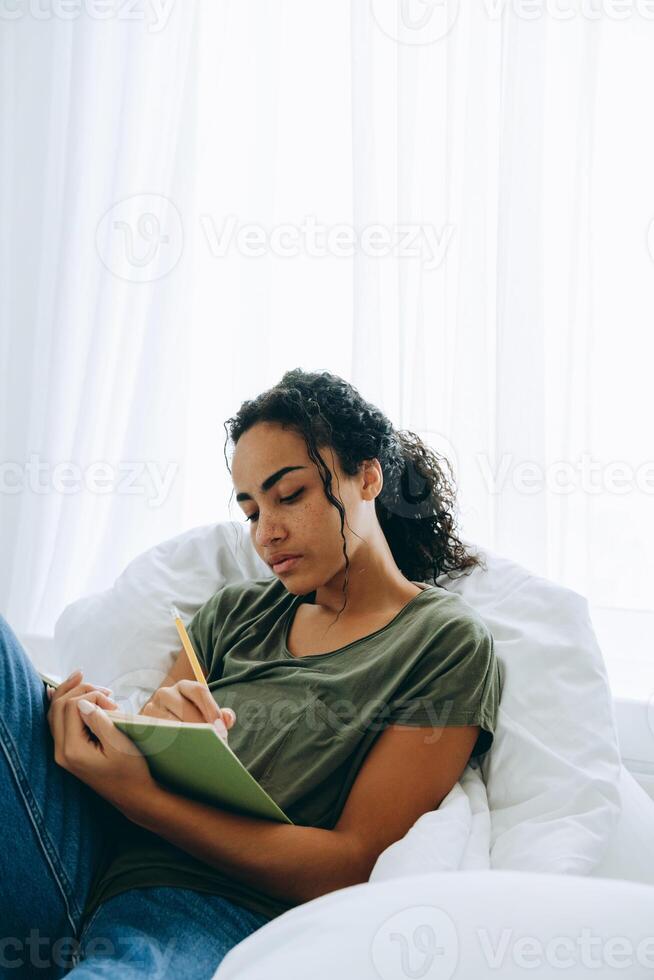 donna africana concentrata che scrive qualcosa nel blocco note sul letto foto