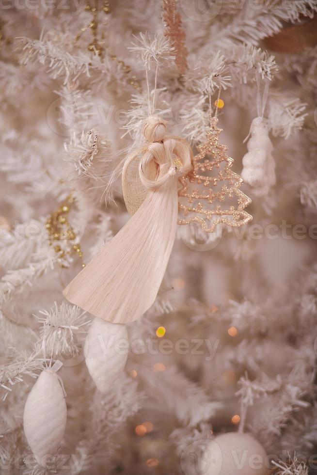 decorazione di un angelo di natale appeso a un ramo illuminato dalle luci scintillanti di un albero di natale bianco foto