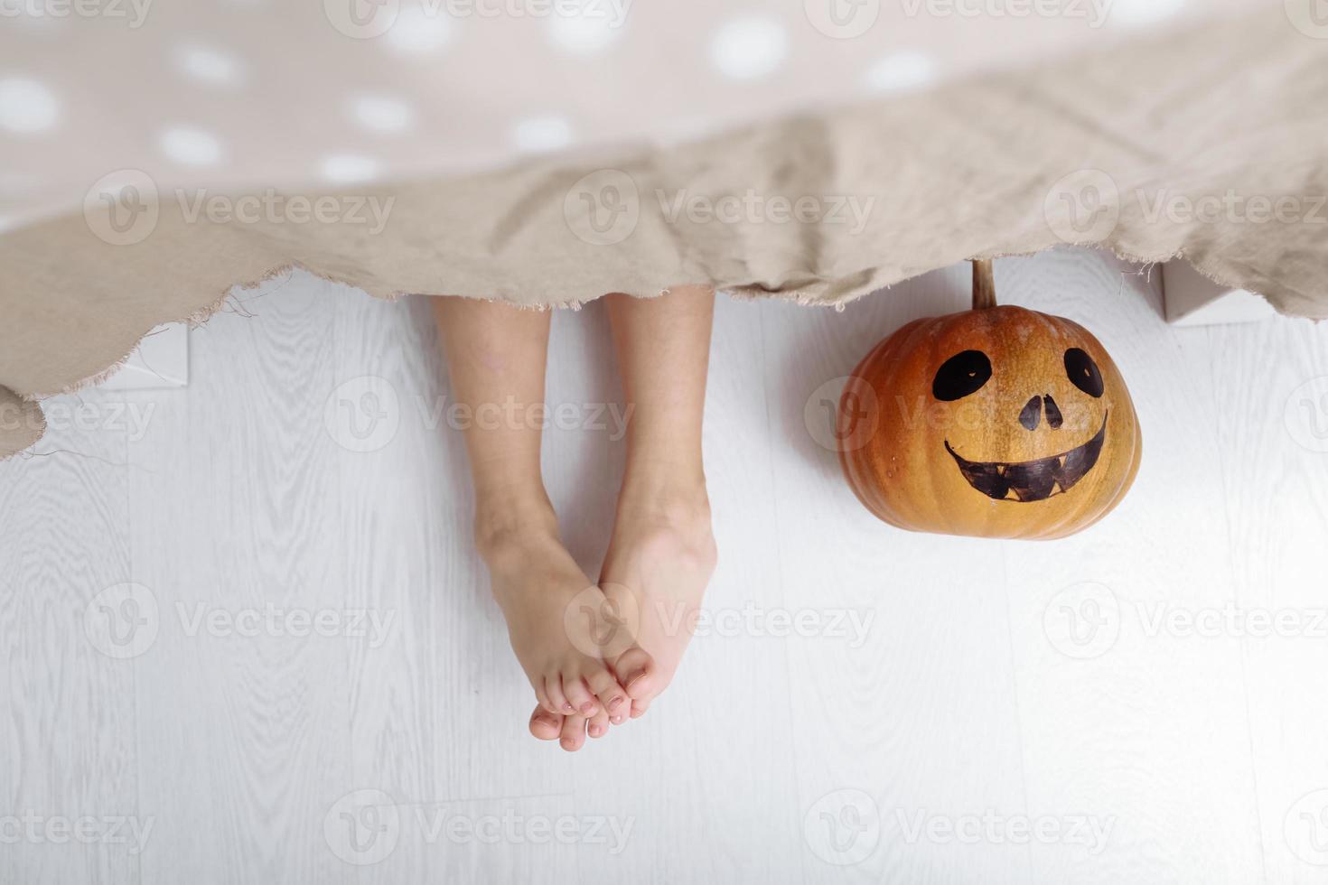 felice Halloween. le gambe di una bambina con la zucca sono sdraiate sul pavimento sotto il tavolo foto