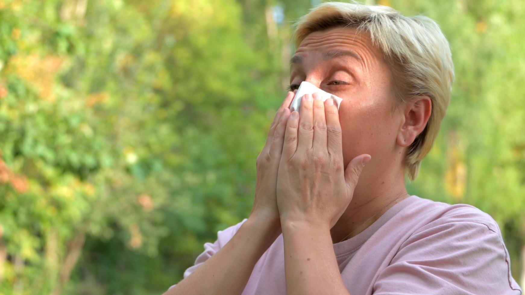 una ragazza con i capelli biondi e un taglio di capelli corto starnutisce per le allergie e si asciuga il naso con un tovagliolo foto