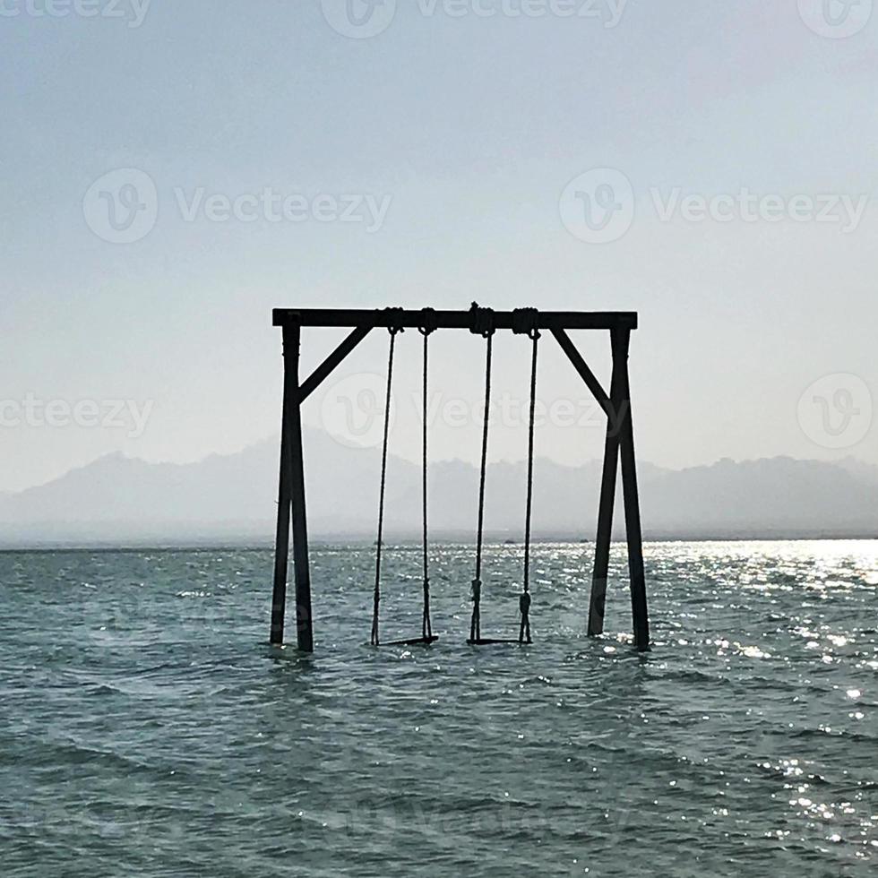 altalena per bambini in legno si trova in un mare calmo blu sotto un cielo pulito e aperto foto