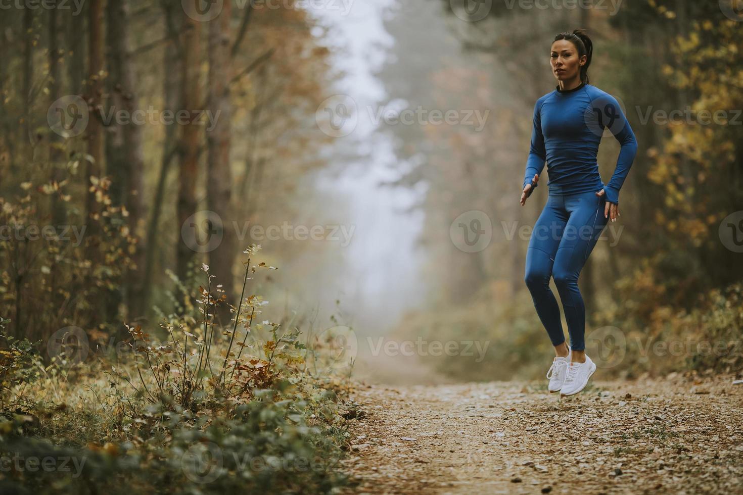 giovane donna che fa il salto in alto sul sentiero nel bosco in autunno foto