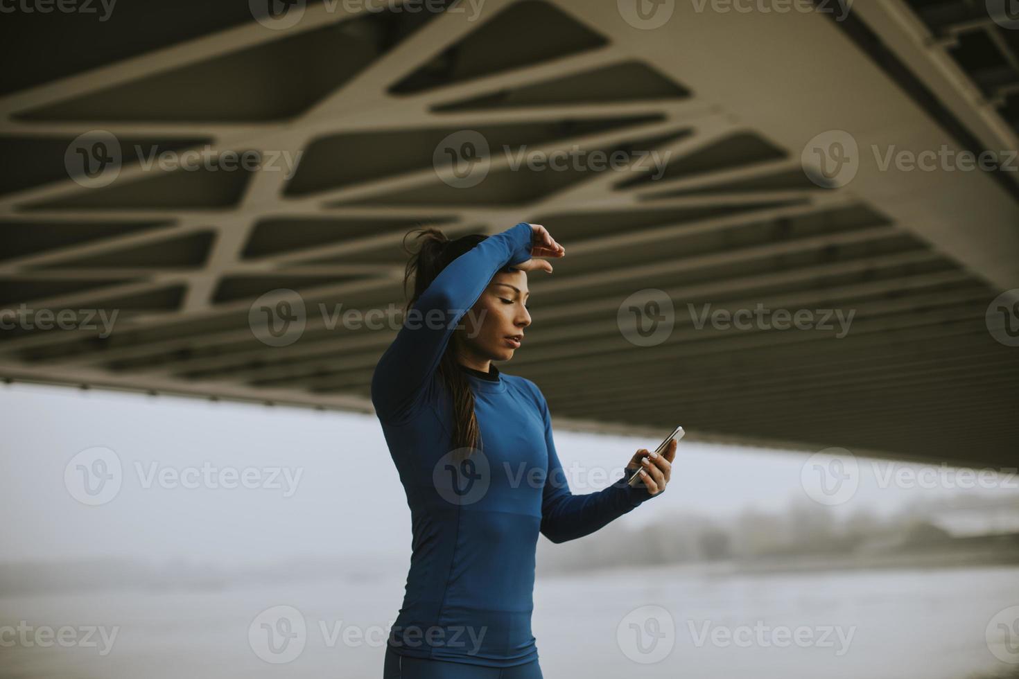 giovane donna in tuta da ginnastica blu che monitora i suoi progressi di allenamento sull'app fitness vicino al fiume al mattino d'autunno foto