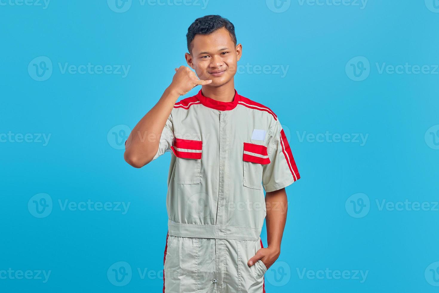 ritratto di sorridente giovane meccanico asiatico che fa il segnale di chiamata su sfondo blu foto