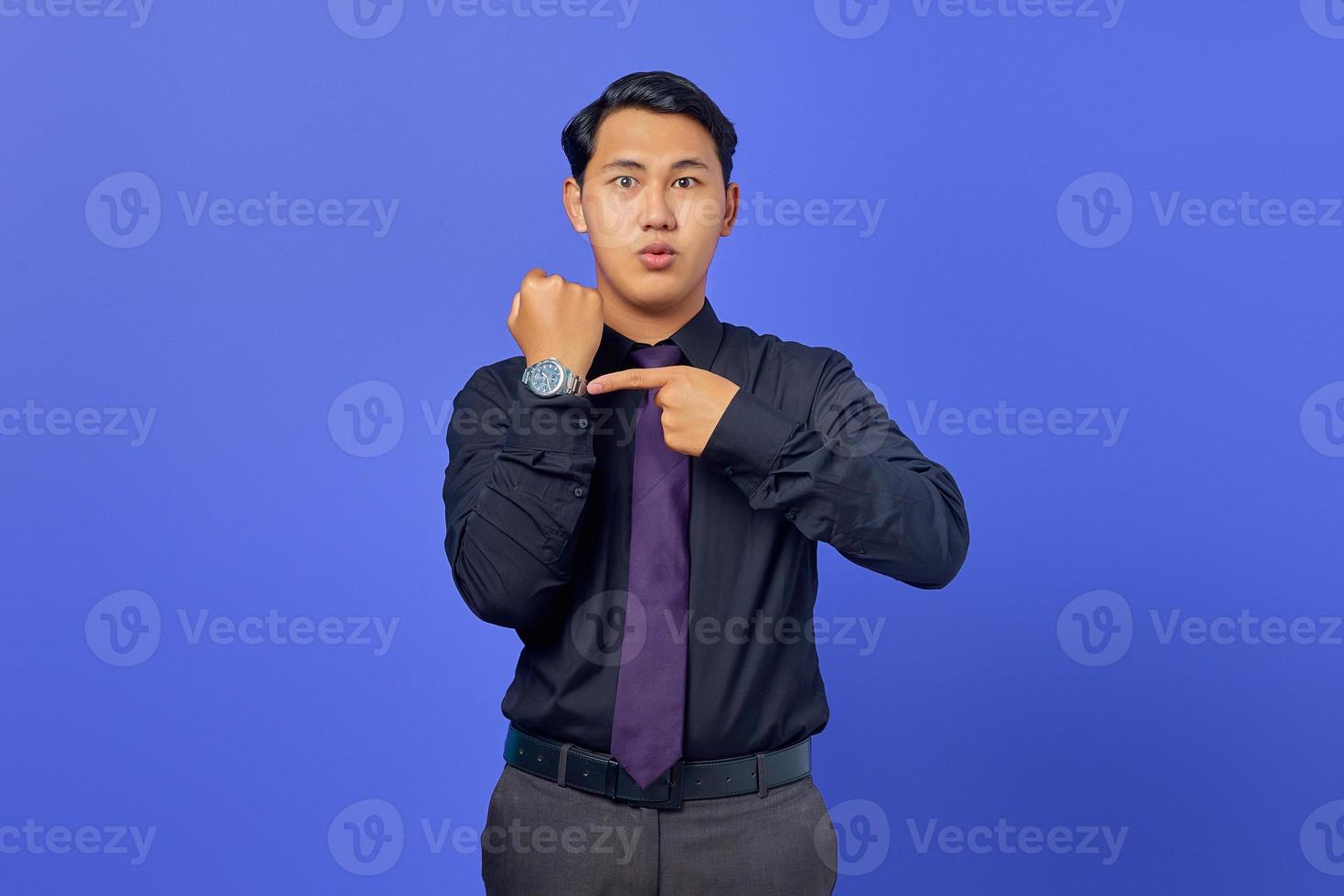 bel giovane uomo d'affari che controlla il tempo sull'orologio da polso su sfondo viola foto