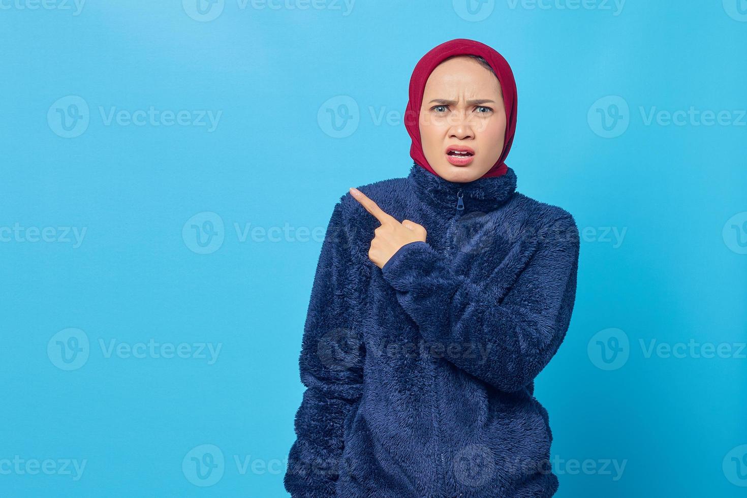 Infastidito giovane donna asiatica che punta lateralmente nello spazio della copia isolato su sfondo blu foto