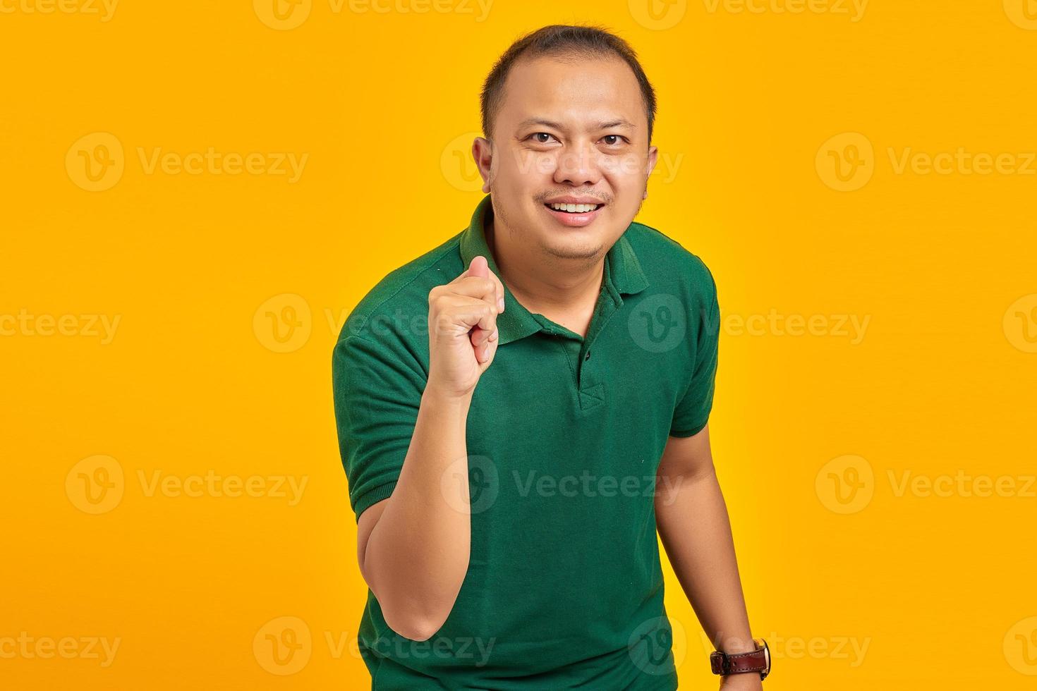 ritratto di un uomo asiatico che mostra il gesto della mano piegando le dita davanti alla telecamera con un'espressione divertente su sfondo giallo foto