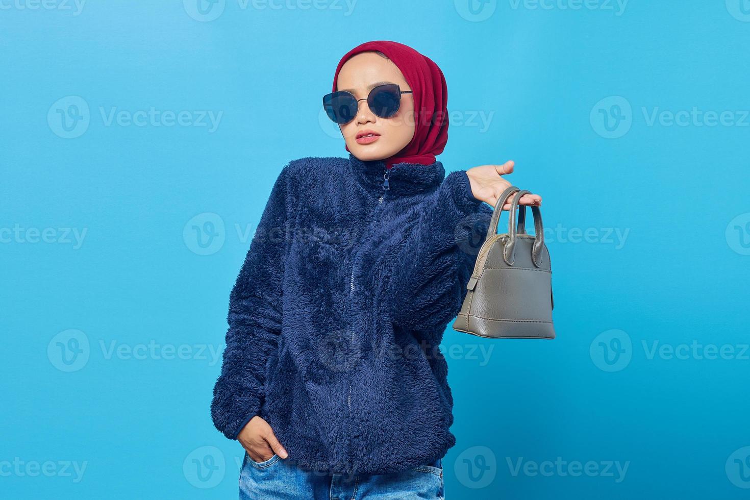 bella giovane donna asiatica che tiene la borsa con un'espressione felice su sfondo blu foto