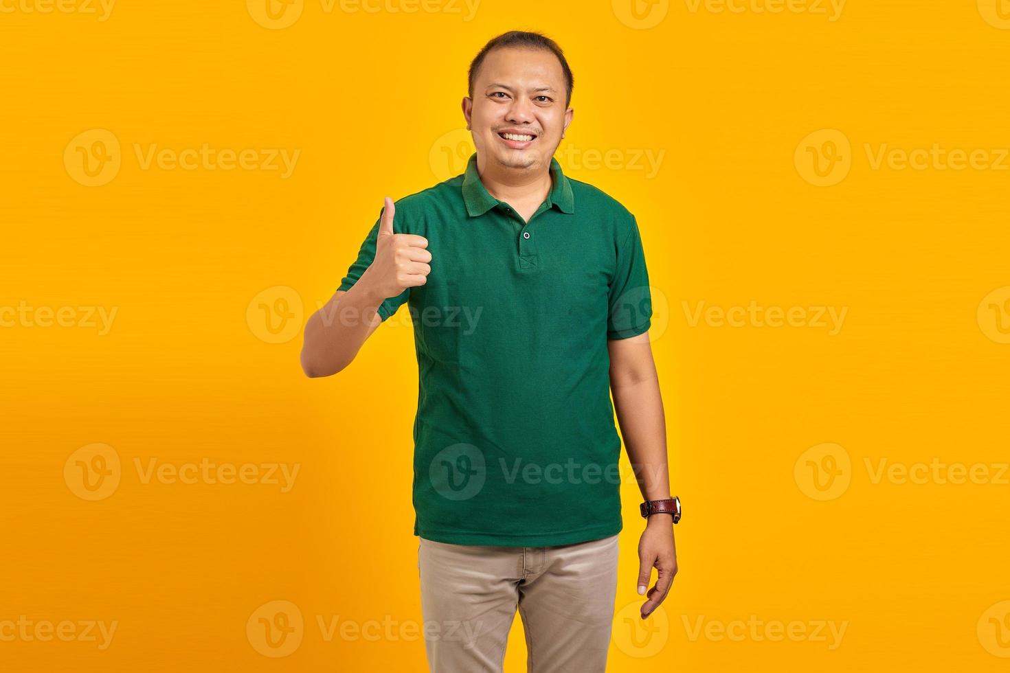 sorridente giovane uomo asiatico che mostra approvazione con il pollice in su gesto su sfondo giallo foto