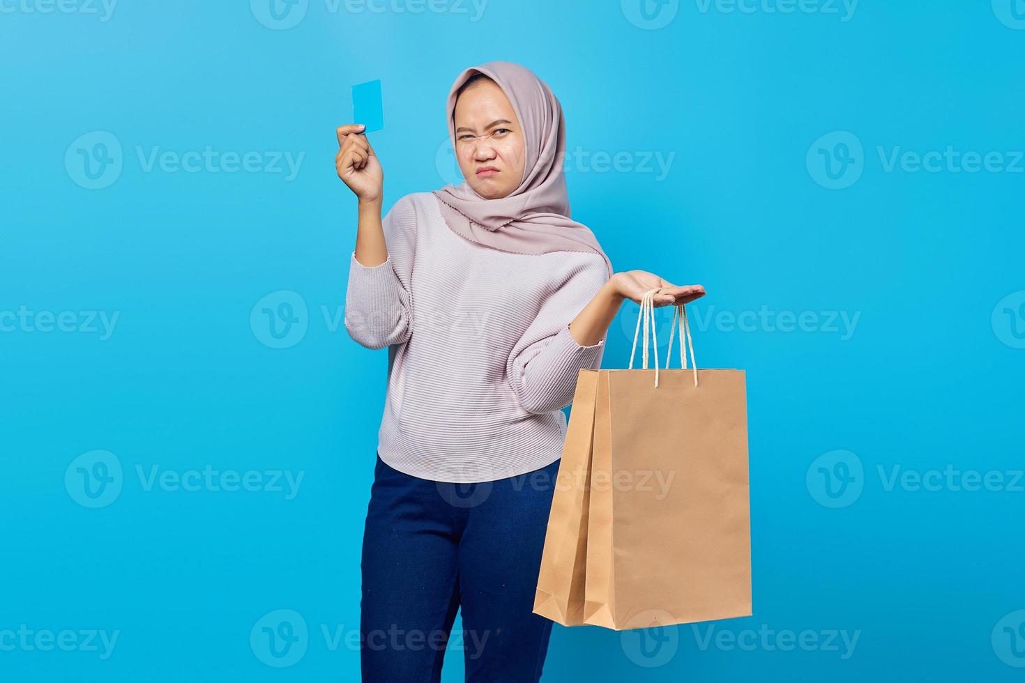 ritratto di una donna asiatica attraente che tiene in mano la borsa della spesa e mostra la carta di credito su sfondo blu foto