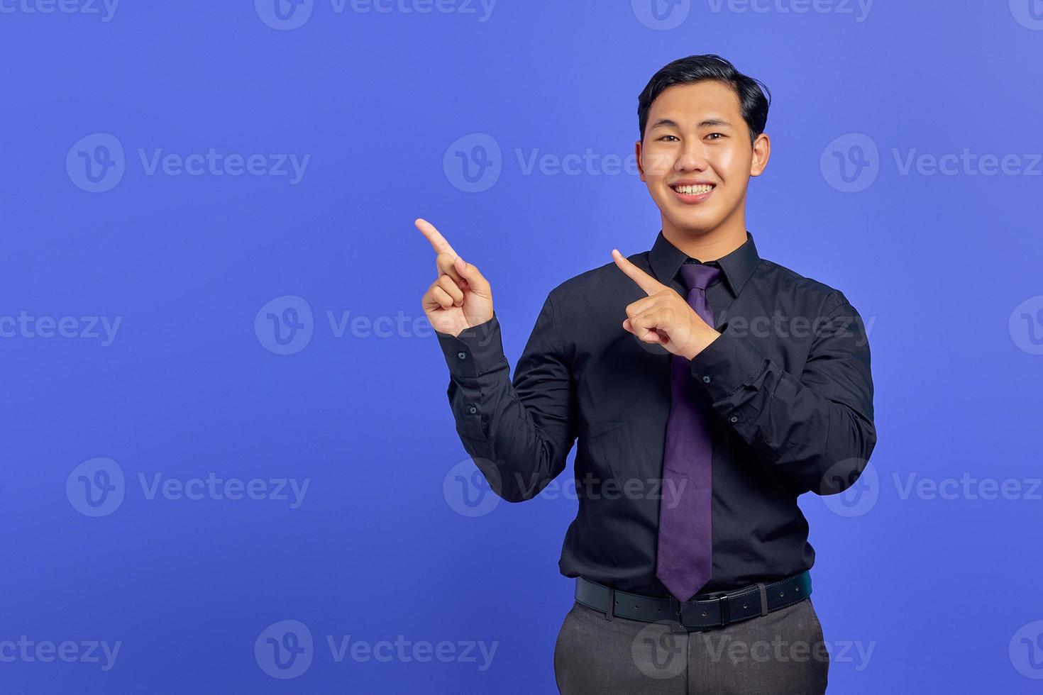 sorridente giovane uomo asiatico che punta il dito contro lo spazio della copia su sfondo viola foto