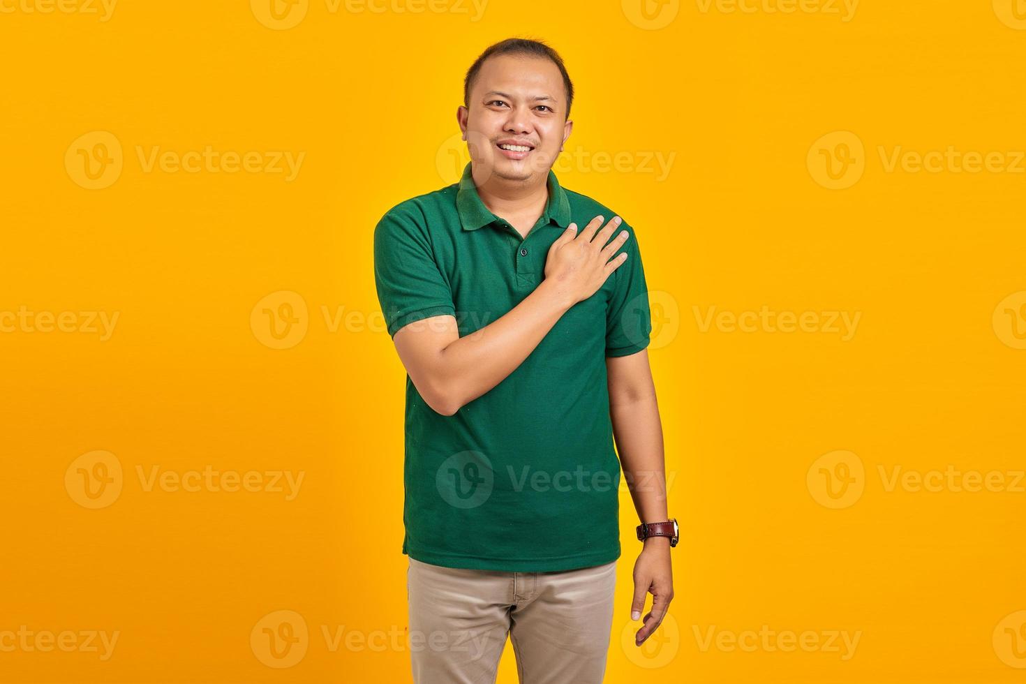 ritratto di un giovane asiatico sorridente che si tiene per mano implorando su sfondo giallo foto