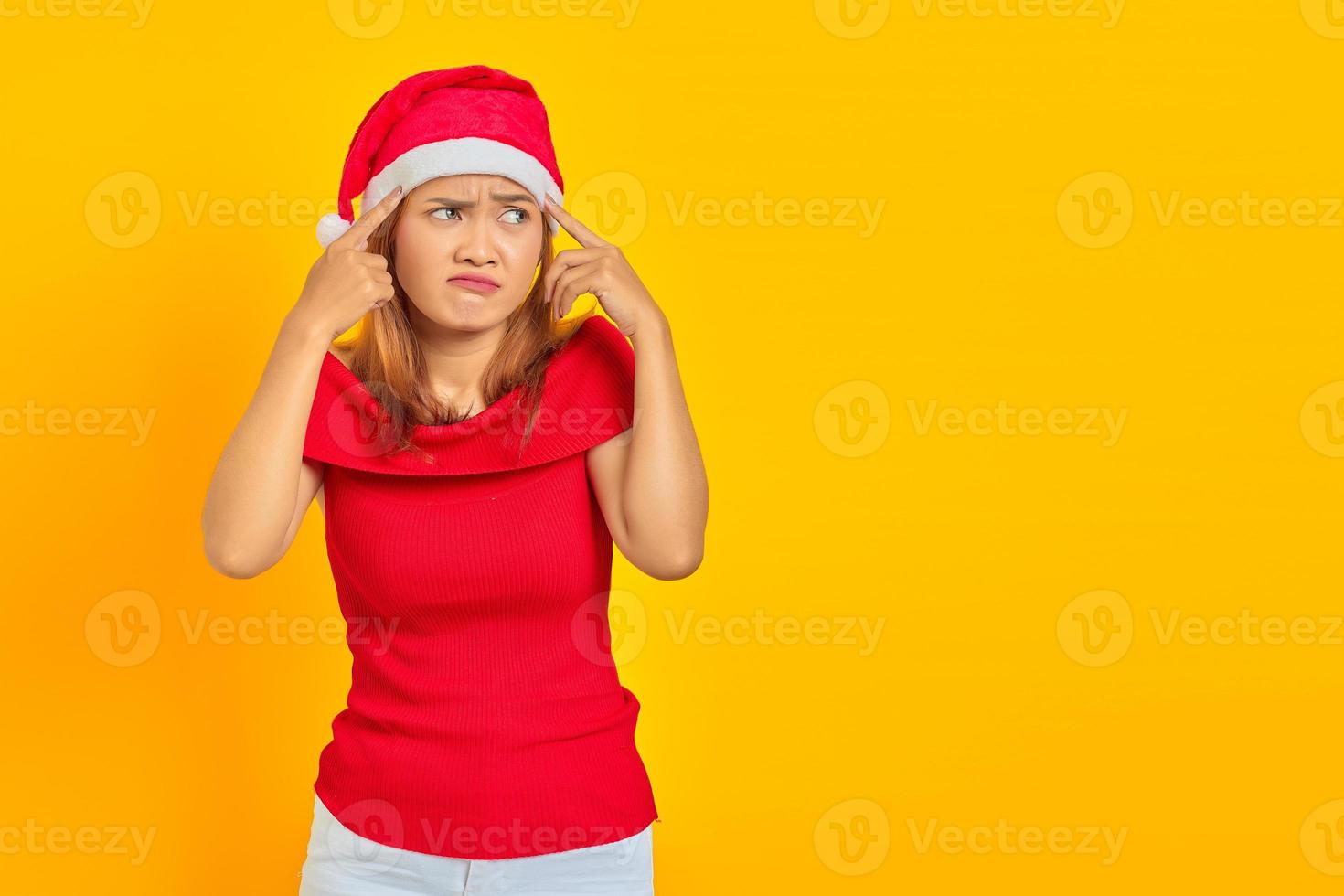 ritratto di una giovane donna pensierosa che indossa un cappello natalizio che ha dubbi e pensa su sfondo giallo foto