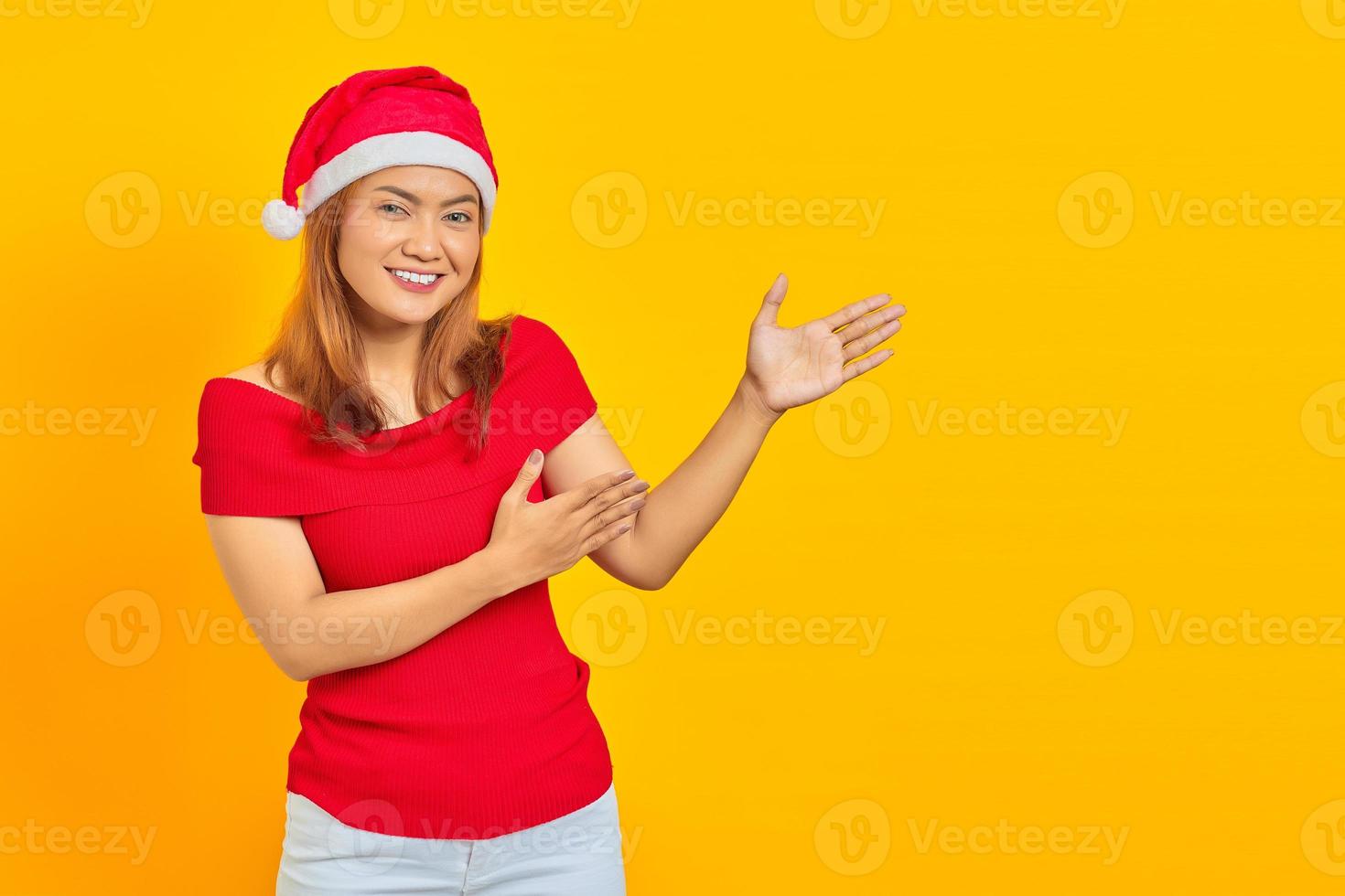 allegra giovane donna che indossa un cappello natalizio e allunga la mano di lato invitando a venire foto