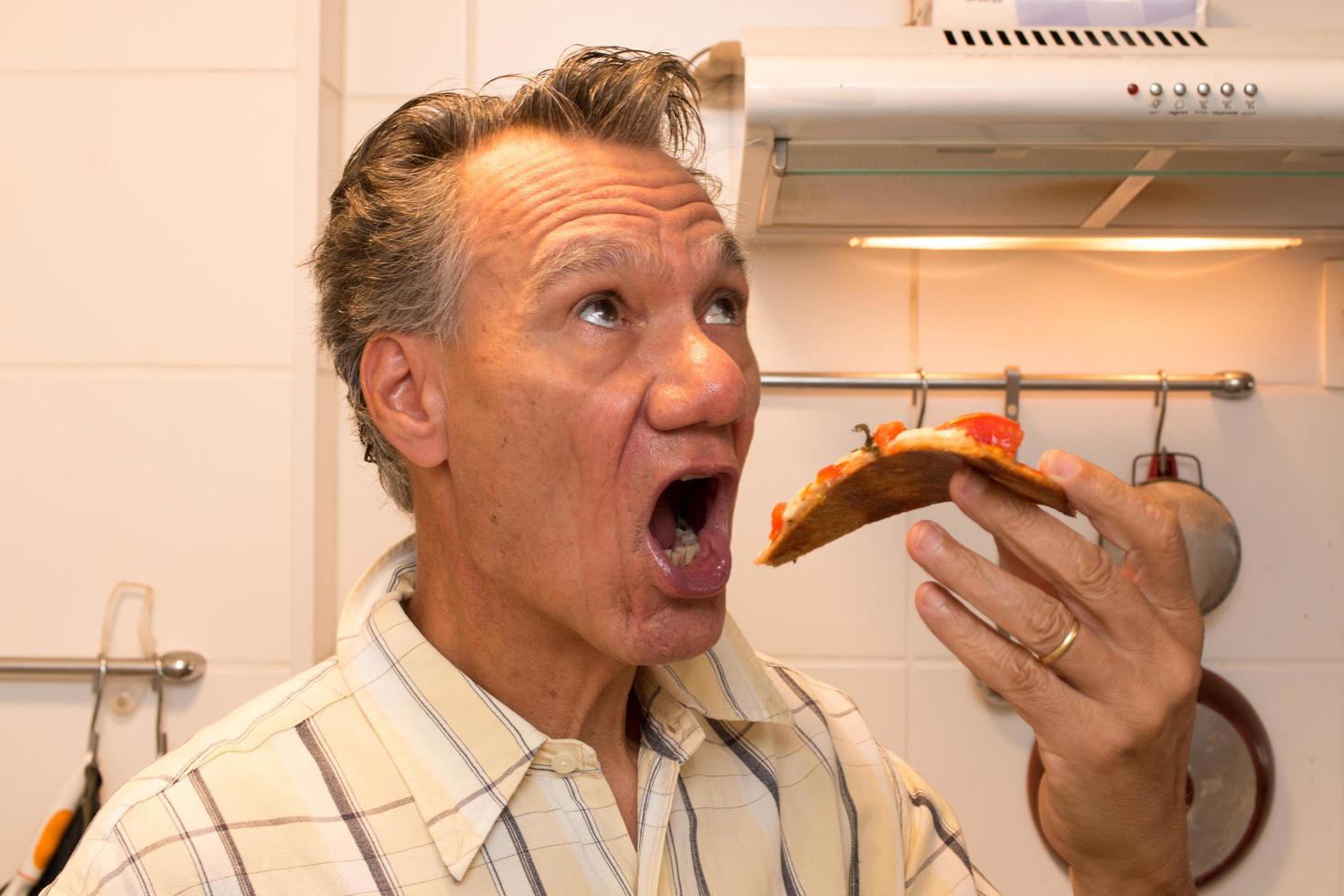 uomo maturo nella sua cucina che mangia pizza margherita fatta in casa foto