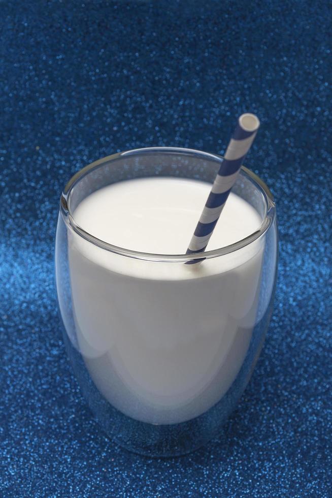 concetto di festa. su uno sfondo blu brillante, un bicchiere di latte con una cannuccia. foto verticale.