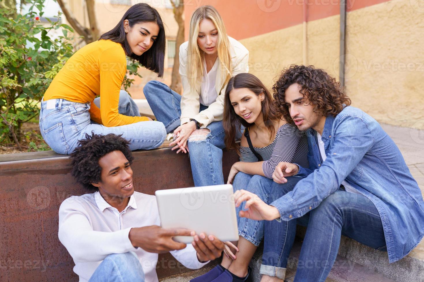 gruppo multietnico di giovani che guardano una tavoletta digitale all'aperto in uno sfondo urbano. foto