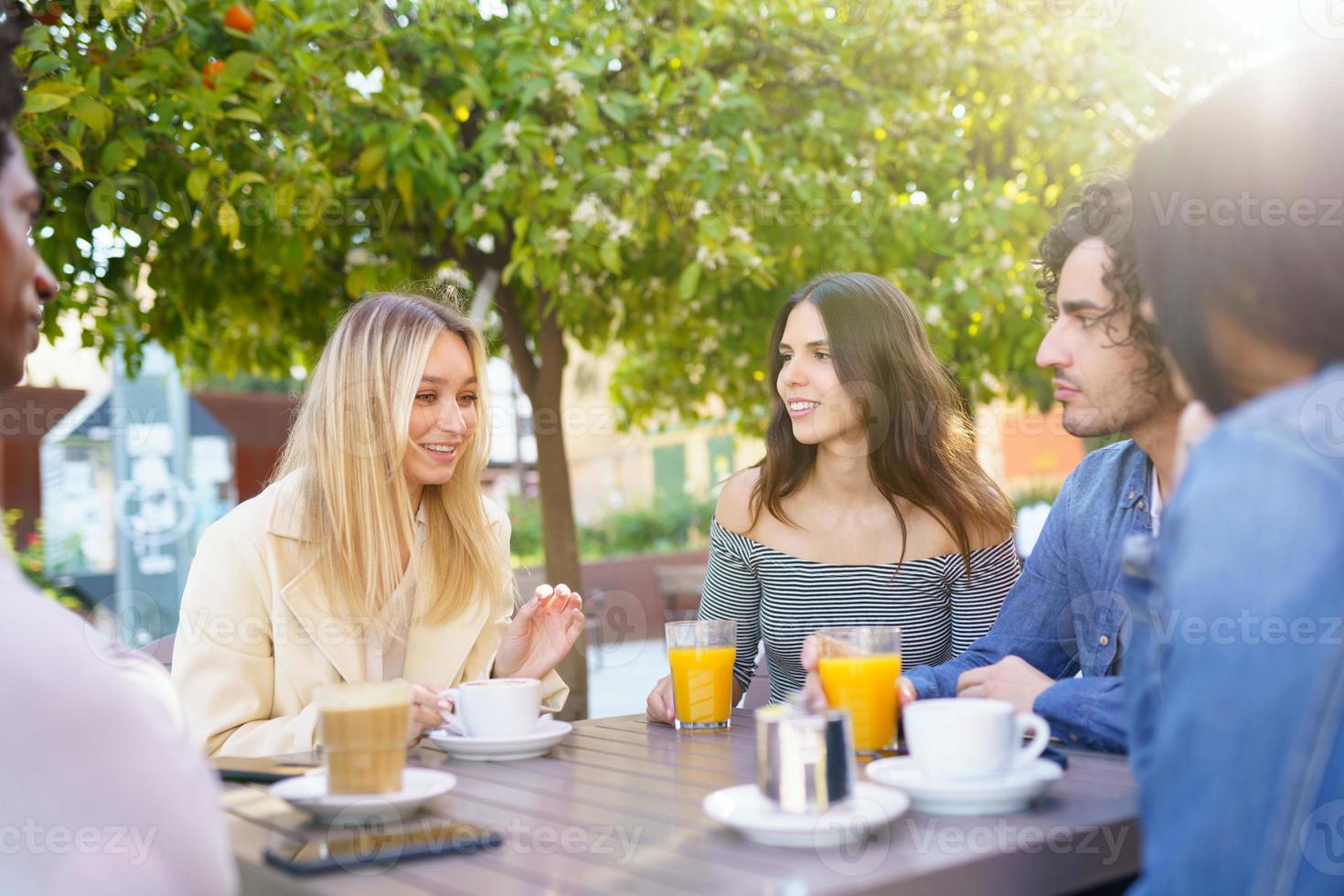 gruppo multietnico di studenti che bevono un drink sulla terrazza di un bar di strada. foto